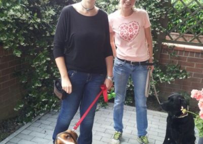 Due donne con un basset hound e un cane nero al guinzaglio in giardino