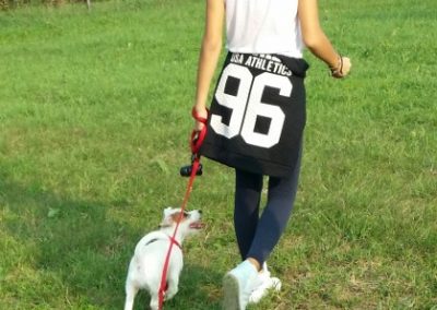 Ragazza cammina al guinzaglio con un piccolo jack russell bianco sul prato