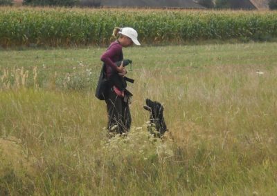 Conduttrice con cappello bianco e cane nero seduto in un prato di campagna