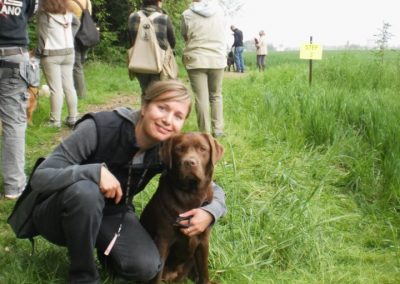 Educatrice accovacciata accanto a un labrador cioccolato durante un raduno all'aperto