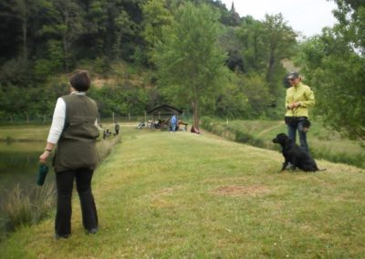 Proprietaria osserva il proprio cane nero seduto vicino al conduttore lungo il laghetto
